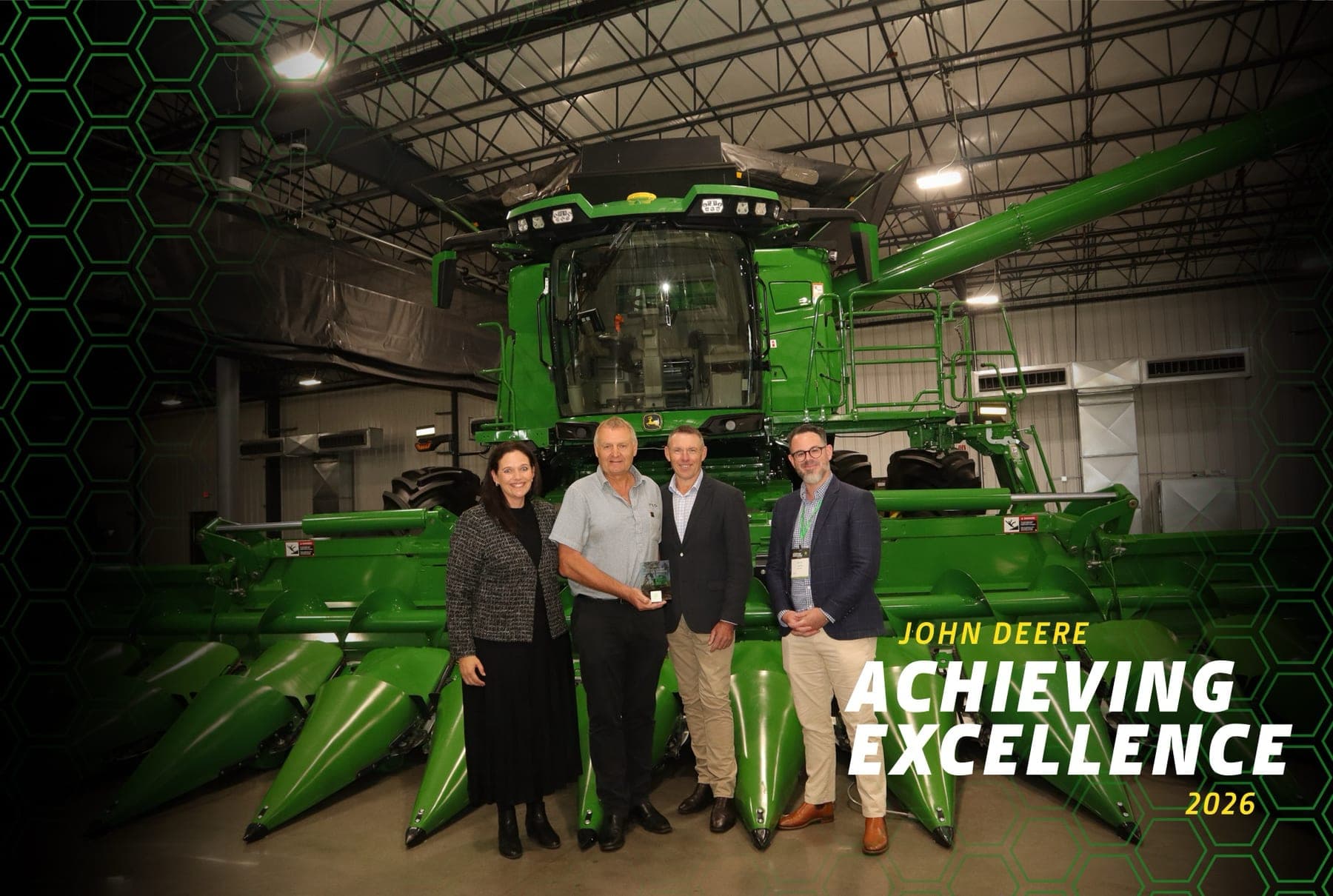 PTS representatives accepting the John Deere Achieving Excellence award, standing in front of a John Deere combine harvester.